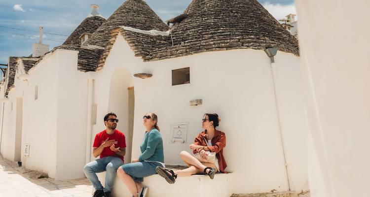 Trois personnes assises devant des maisons traditionnelles en pierre rondes.
