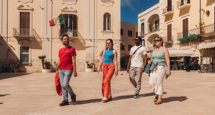 Quatre personnes marchent dans une piazza italienne. Un drapeau italien est visible.