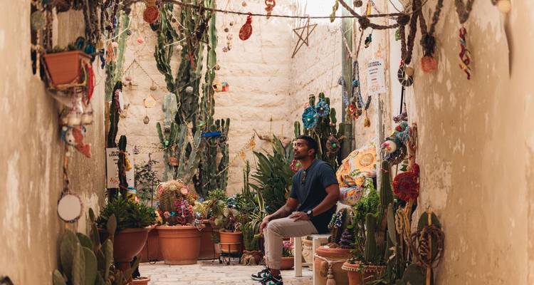Un homme assis dans une ruelle étroite décorée de plantes et d'art.