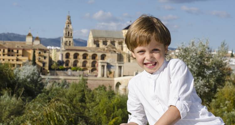 Kind glimlacht met een historisch gebouw op de achtergrond.