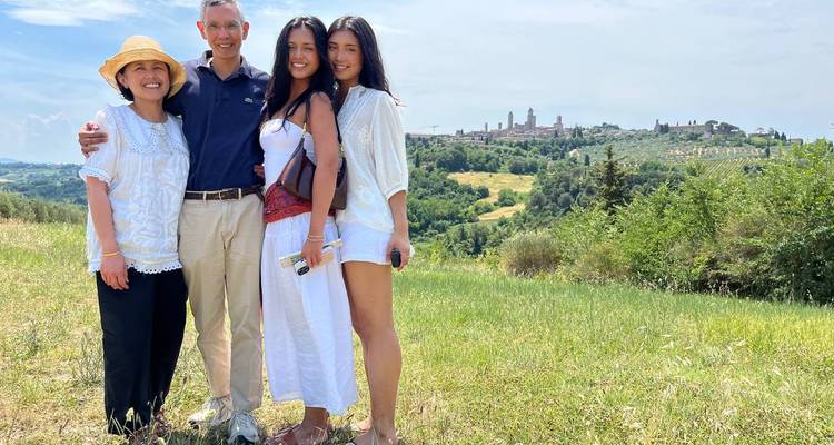 La familia posando juntos en una ladera cubierta de pasto con el horizonte del pueblo toscano de fondo