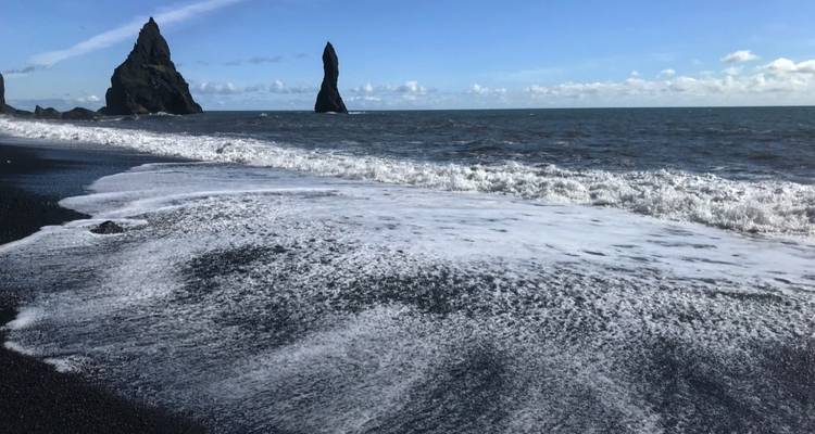 Olas llegando a una playa de arena negra con formaciones rocosas.