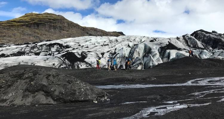 Personas haciendo senderismo en un glaciar con alrededores rocosos y cielo nublado.