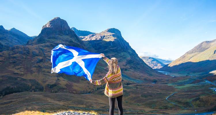 Une personne tenant un drapeau écossais sur un fond de montagnes.