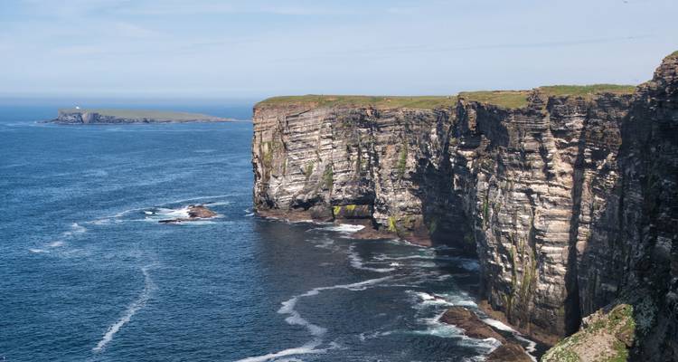 Falaises surplombant la mer avec un phare au loin.
