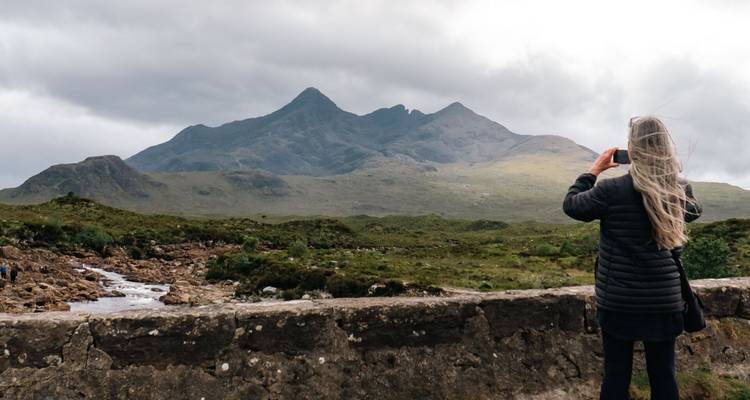 Une femme photographiant un paysage montagneux avec des pics escarpés.