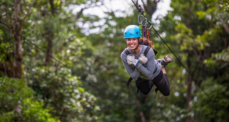 Vrouw in een blauwe helm zoeft over een zipline door de weelderige Costa Ricaanse regenwoudkroon.
