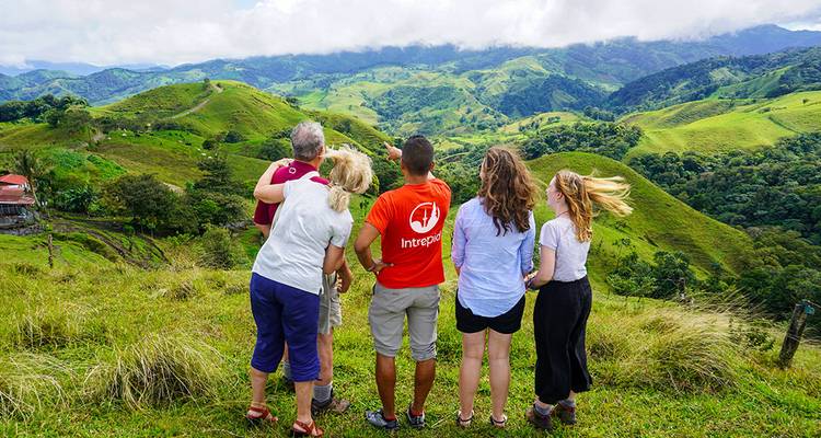 Gids in Intrepid-shirt wijst een groep aandachtige bezoekers op een panoramisch groen dal.