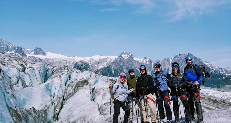 Groupe de randonneurs posant sur un glacier avec des montagnes en arrière-plan.