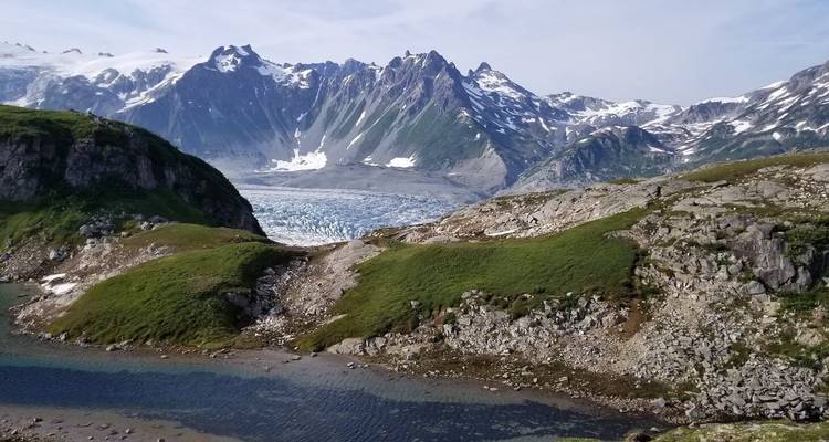 Collines vertes et terrain rocheux entourant un glacier lointain.