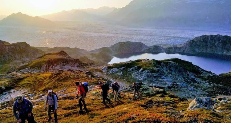 Des randonneurs gravissant une colline avec un éclairage de lever de soleil sur une plaine glaciaire au loin.