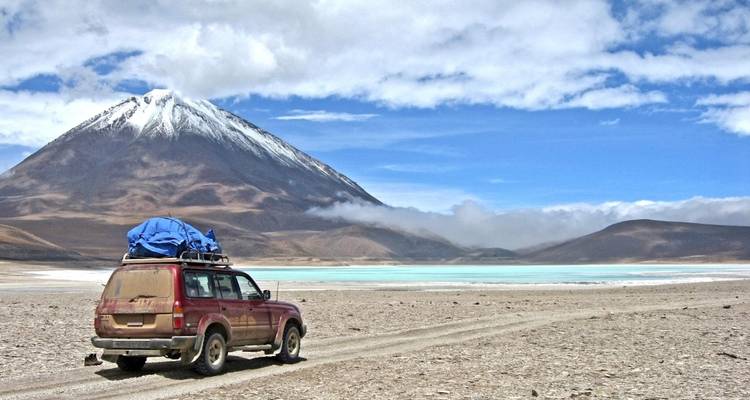 A car driving on a barren road with a snow-capped mountain in the distance.