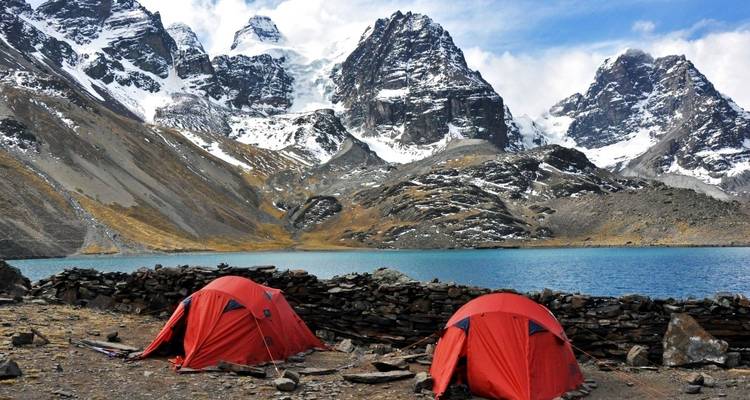 Tents by a lake with snowy mountains in the background.