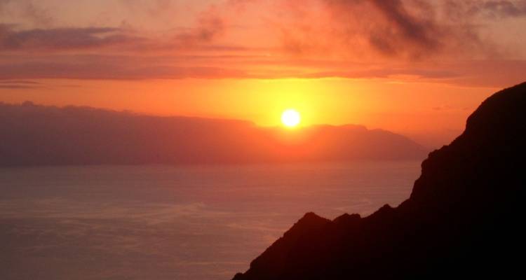 Vista del atardecer sobre el océano con montañas en silueta.