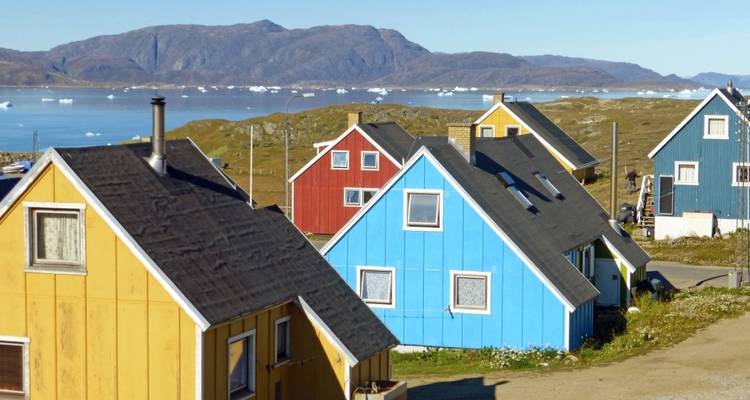 Colorful houses on a coastal landscape with visible icebergs.