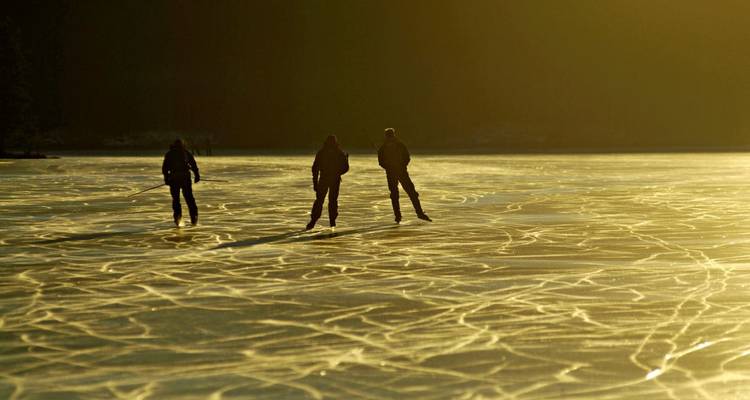 Silhouetten van drie schaatsers glijden over goudkleurige door zonsondergang verlichte gebarsten ijspatronen.
