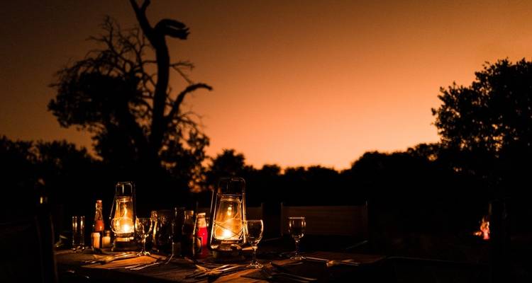 Lantern-lit dinner setting under an orange sky.