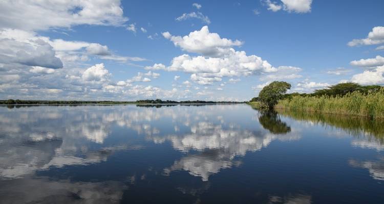 Serene river view with fluffy clouds reflecting on the water.