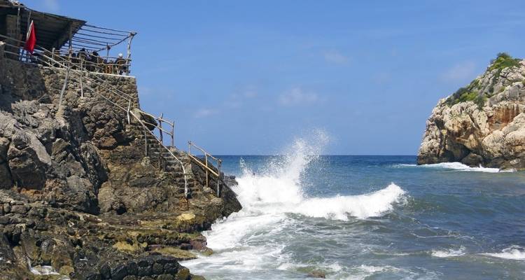 Des vagues qui se brisent contre un rivage rocheux avec une petite structure en bois.