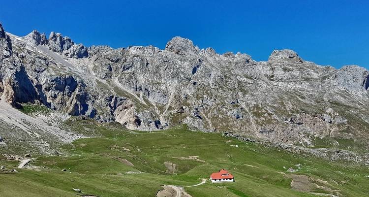 Berglandschap met een enkel huis en rotsachtige toppen onder een heldere blauwe hemel.
