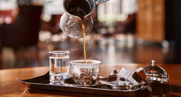 Traditional Turkish coffee being poured with lokum on the side.