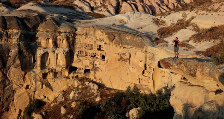 Person on a scenic overlook with rock dwellings in the background.