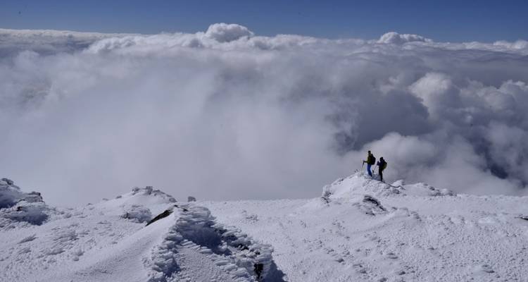 Dos personas de pie en una cima cubierta de nieve con nubes.