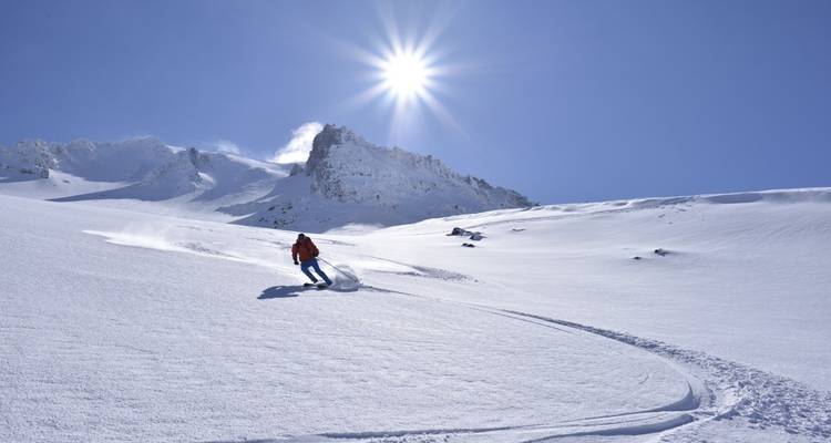 Skifahrer auf einem schneebedeckten Hang mit Sonne am klaren blauen Himmel.