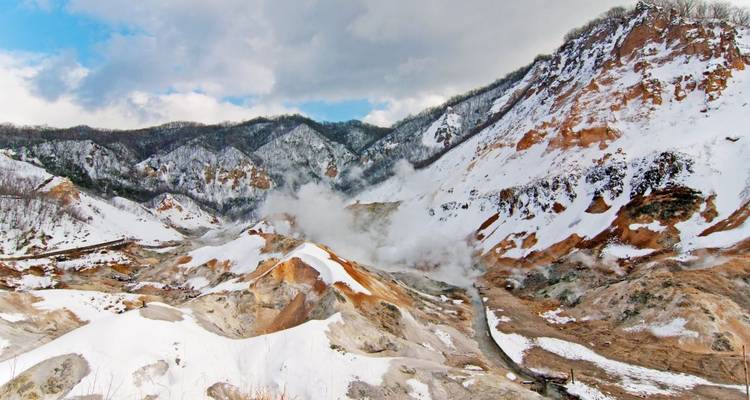 De la vapeur s'élève du paysage géothermique d'une vallée en hiver.