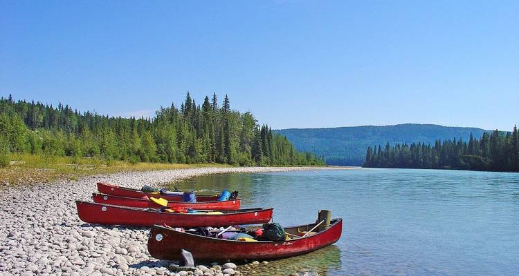 Rote Kanus auf einem Kieselstrand neben einem Fluss mit Wäldern und Hügeln.
