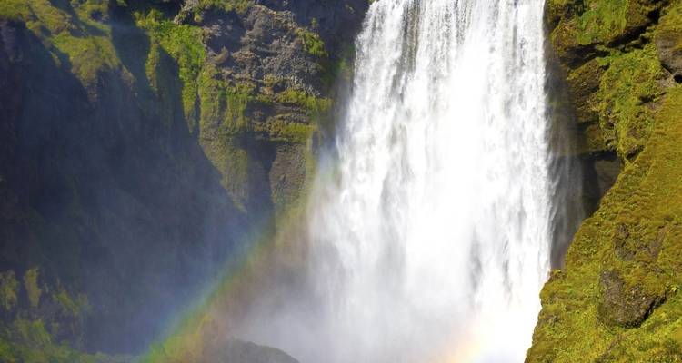Waterval die naar beneden valt over bemoste rotswanden met een zichtbare regenboog.