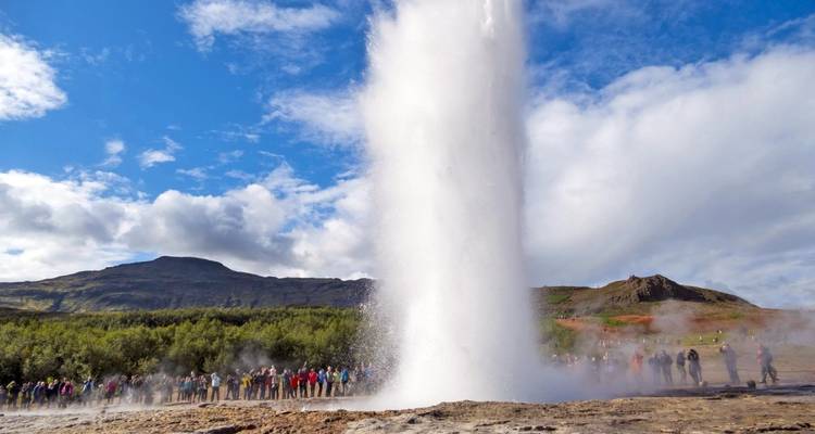 Geiser die uitbarst met een menigte die toekijkt, onder een heldere blauwe hemel.