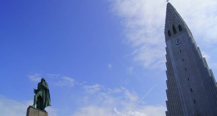 Kerktoren en standbeeld onder een blauwe hemel, gefotografeerd in verticale oriëntatie.