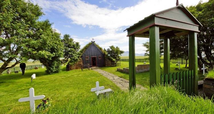 Kleine traditionele IJslandse kerk omgeven door een weelderig groen landschap en begraafplaats.