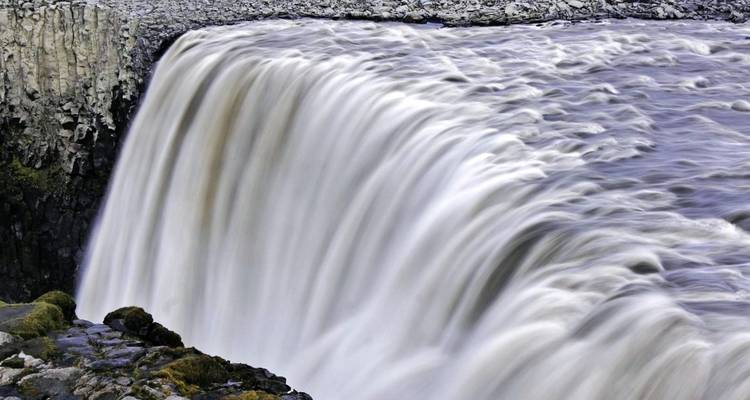 Brede waterval met een sterke stroming over rotsachtig terrein.
