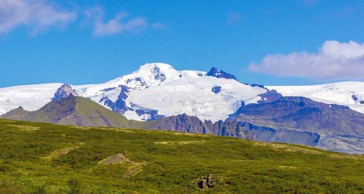 Sneeuwbedekte bergen met een groene vallei op de voorgrond.