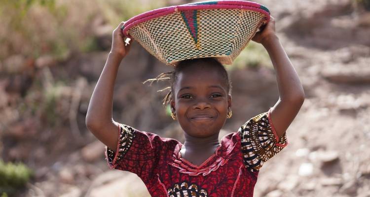Enfant souriante avec un panier coloré sur la tête.