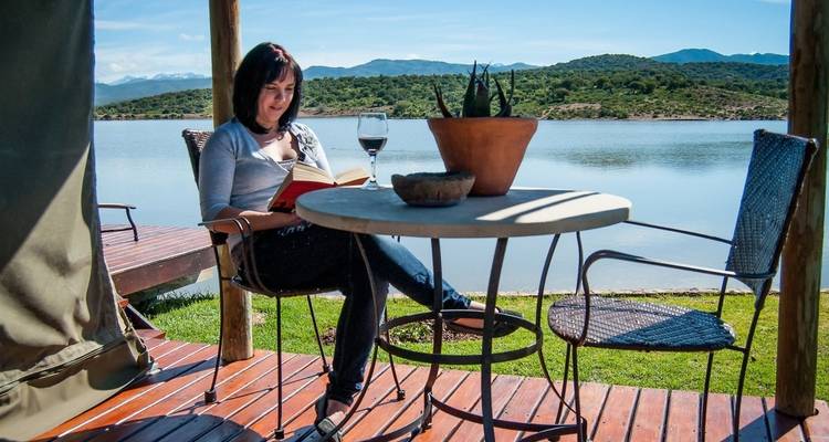 Woman relaxing by a lake with a book and a glass of wine.