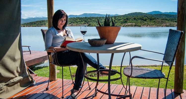 Woman reading at a lakeside with a view of mountains.