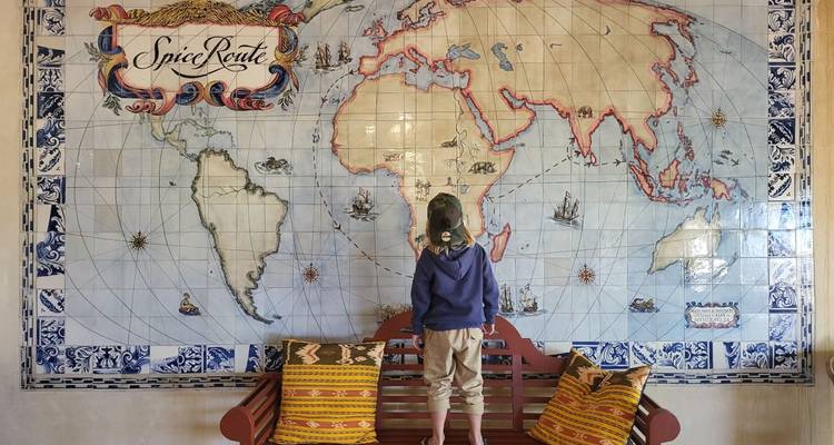 Child standing on a bench looking at a large map of the world.