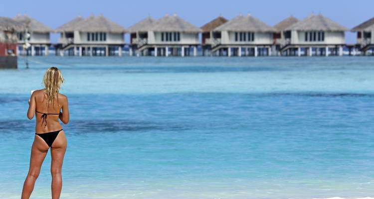 Person standing on a beach looking at overwater bungalows.