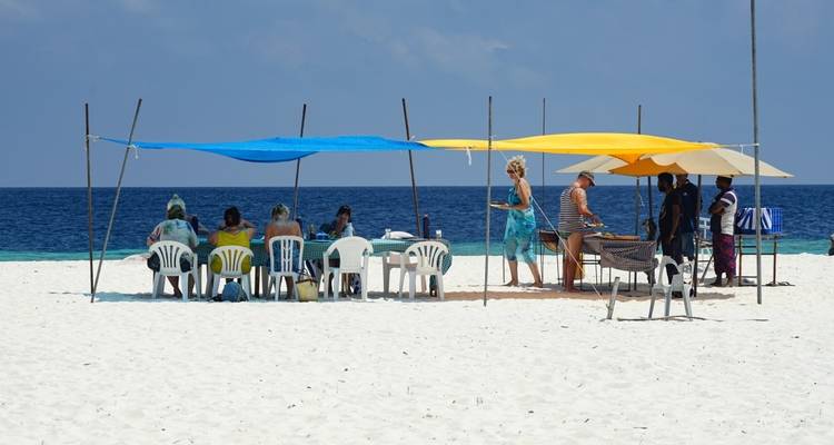 Group of people seated under colorful canopies on a beach.