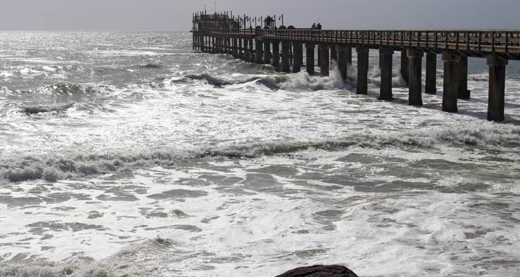Des vagues de l'océan frappant une longue jetée avec des gens au bout.