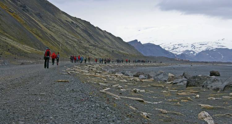 Groupe de randonneurs marchant le long d'un littoral accidenté avec des montagnes en arrière-plan.