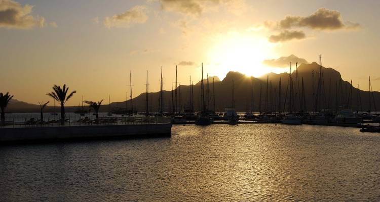 Vue du coucher de soleil d'une marina avec des voiliers et des montagnes.