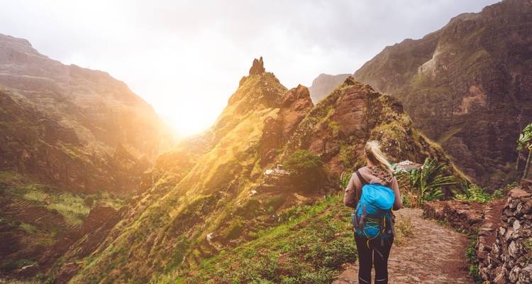 Personne marchant sur un sentier de montagne au coucher du soleil avec un éclairage dramatique