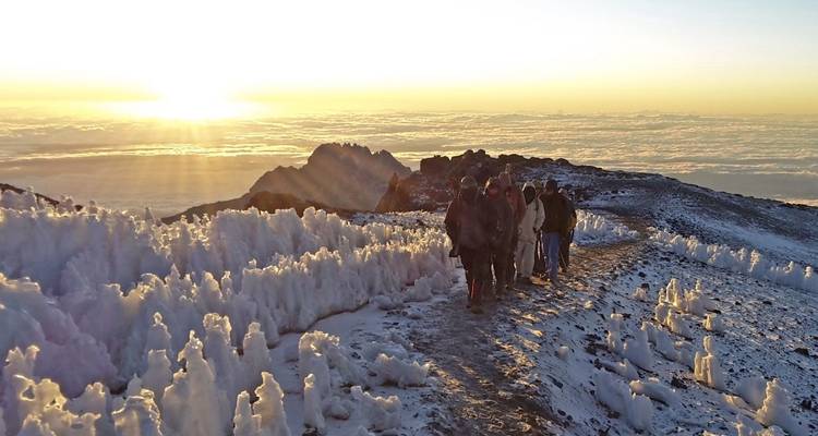 Grupo caminando por un sendero nevado con un amanecer de fondo.