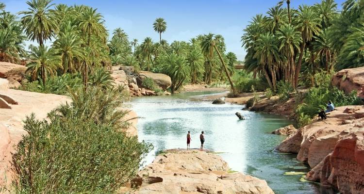 People near a river in a lush oasis landscape.