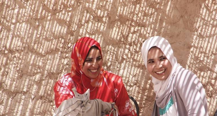 Two women smiling sitting in the shade.