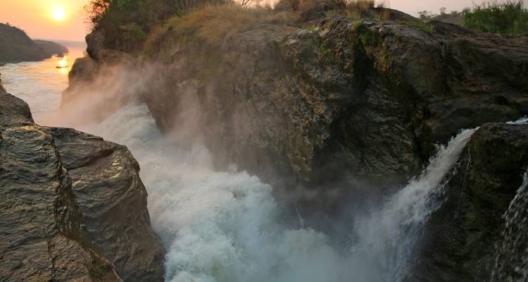 Majestic waterfall with mist and a river during sunset.